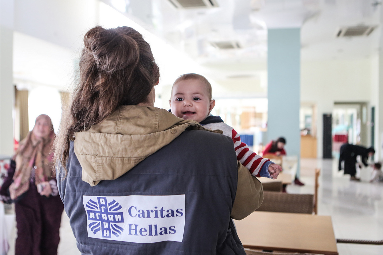Aid worker carrying baby at Caritas hotel in Lesbos. Photo by Lefteris Partsalis, Caritas Switzerland